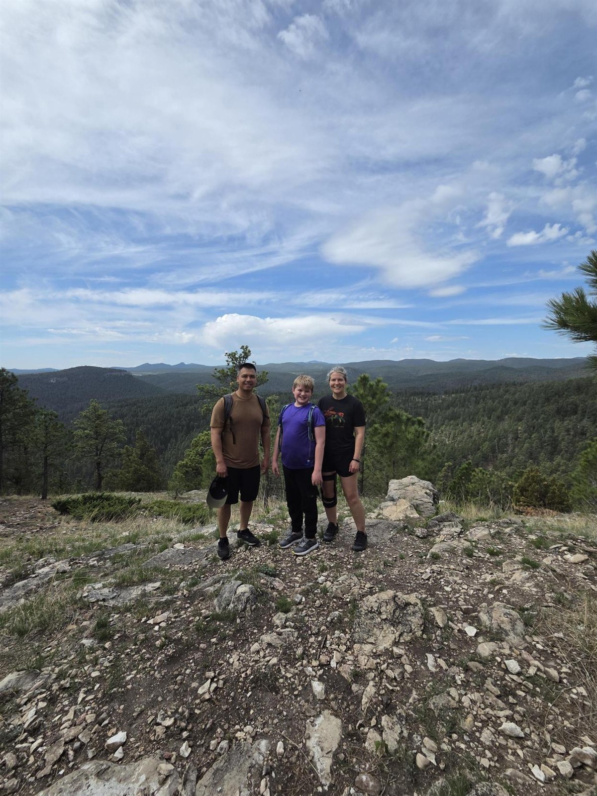 A Big, Little, and parent hiking on a ridge overlooking the Black Hills